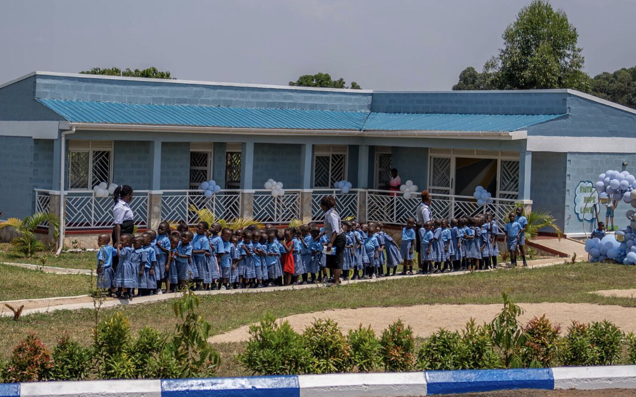 Der Kindergarten in Mityana: ein langgestrecktes blaues Gebäude mit Veranda, davor die Kinder in ihren Schuluniformen