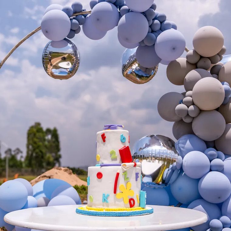 Zweistöckige Torte mit bunten Buchstaben unter einem Ballonbogen vor dem Kindergartengebäude