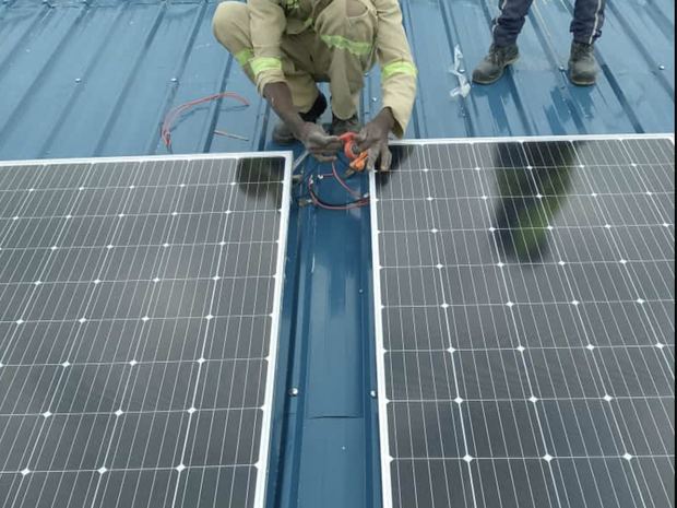 Ein Monteur verschraubt Solarmodule auf dem blauen Blechdach des Kindergartens